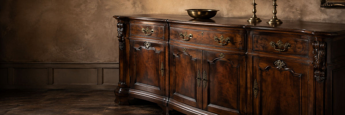 Antique wooden sideboard with paneled doors, ornate brass hardware, candlesticks and a decorative brass bowl.