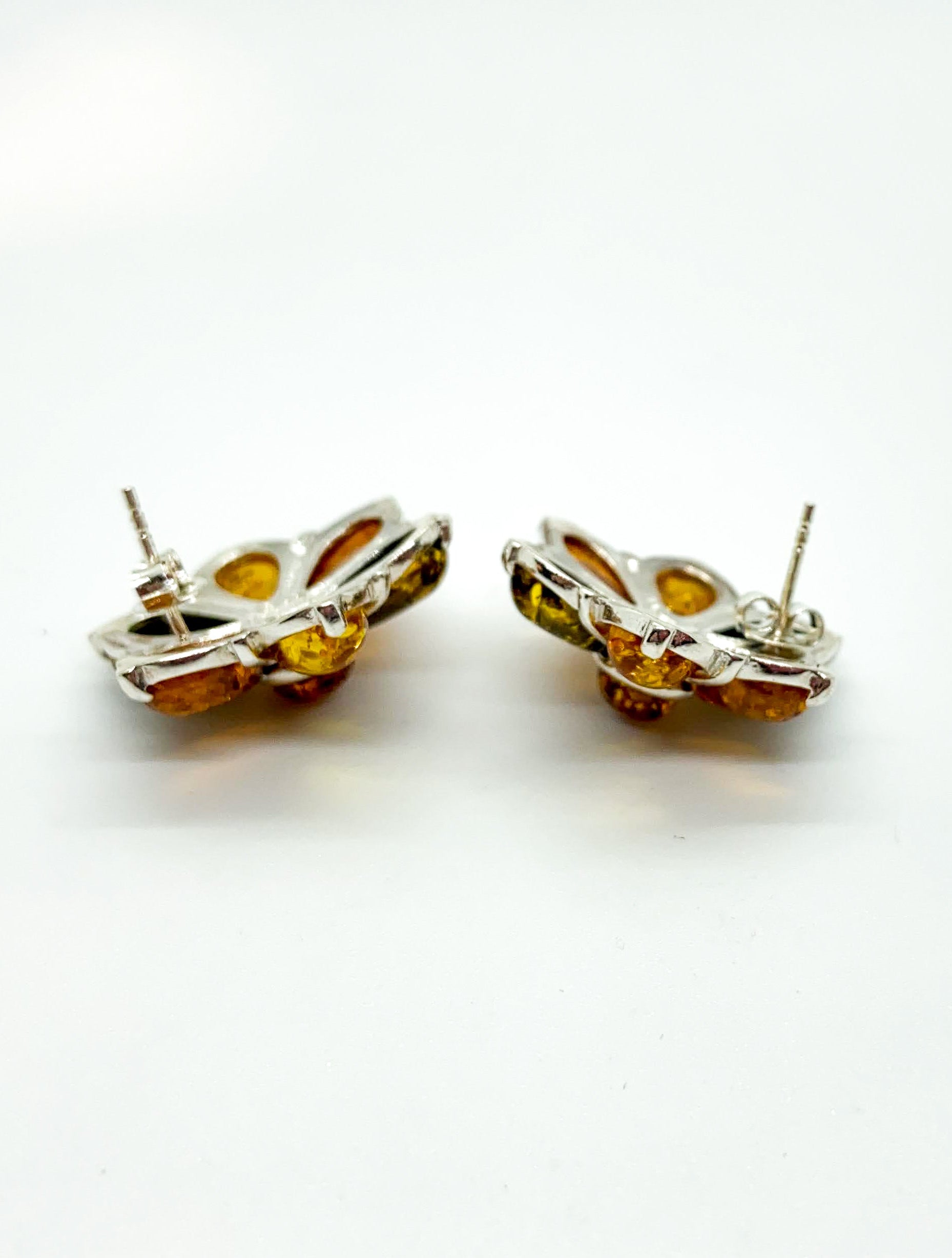 A pair of silver-toned flower stud earrings with amber-colored inlay, shown from the back on a plain white background.