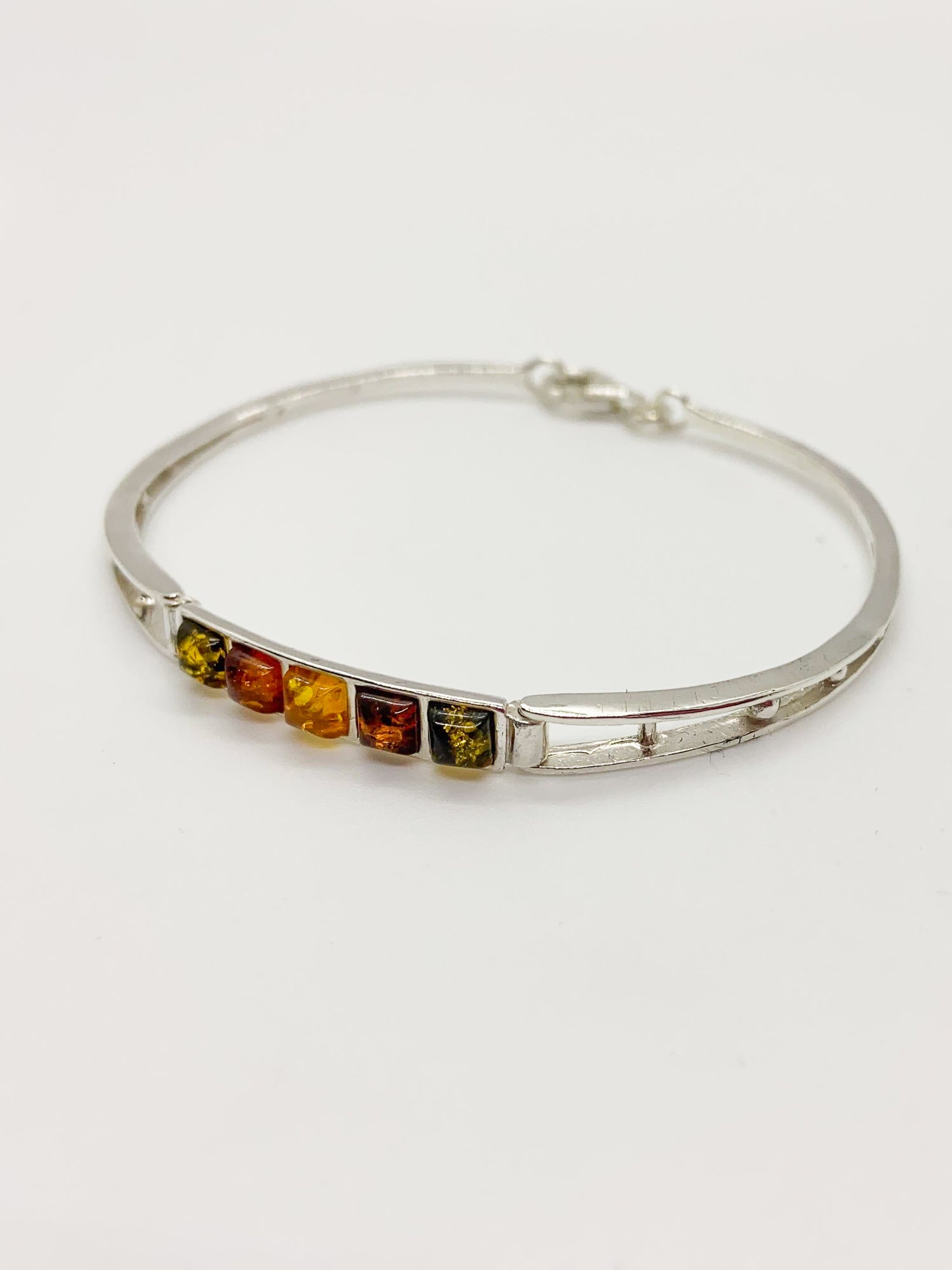 A sterling silver bangle bracelet featuring a row of small square-cut amber stones in yellow, orange, and brown, displayed on a clean white background.