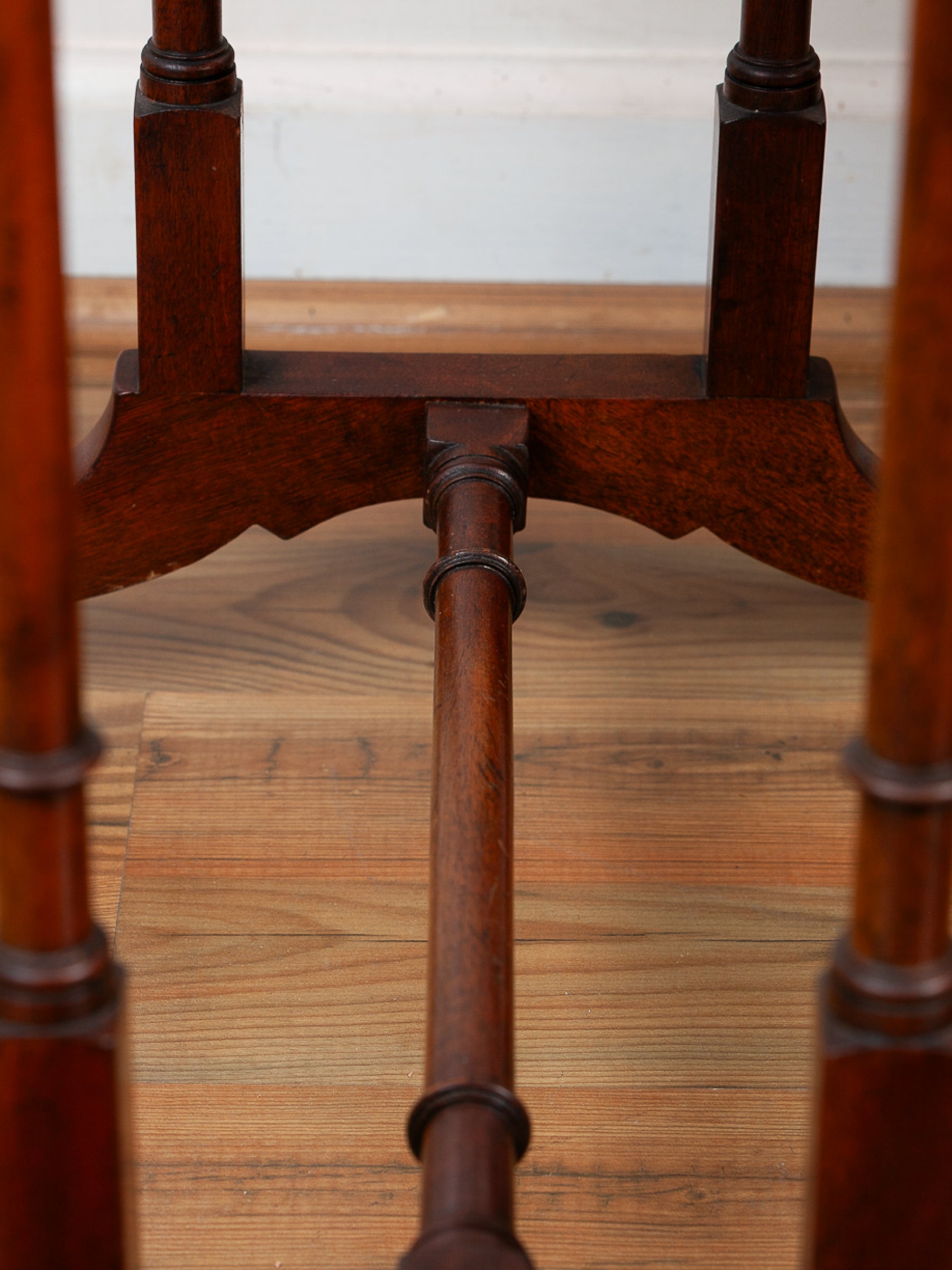 Close-up of the base and central support post of a dark brown wooden table, showing the joinery and grain on a light wood floor.