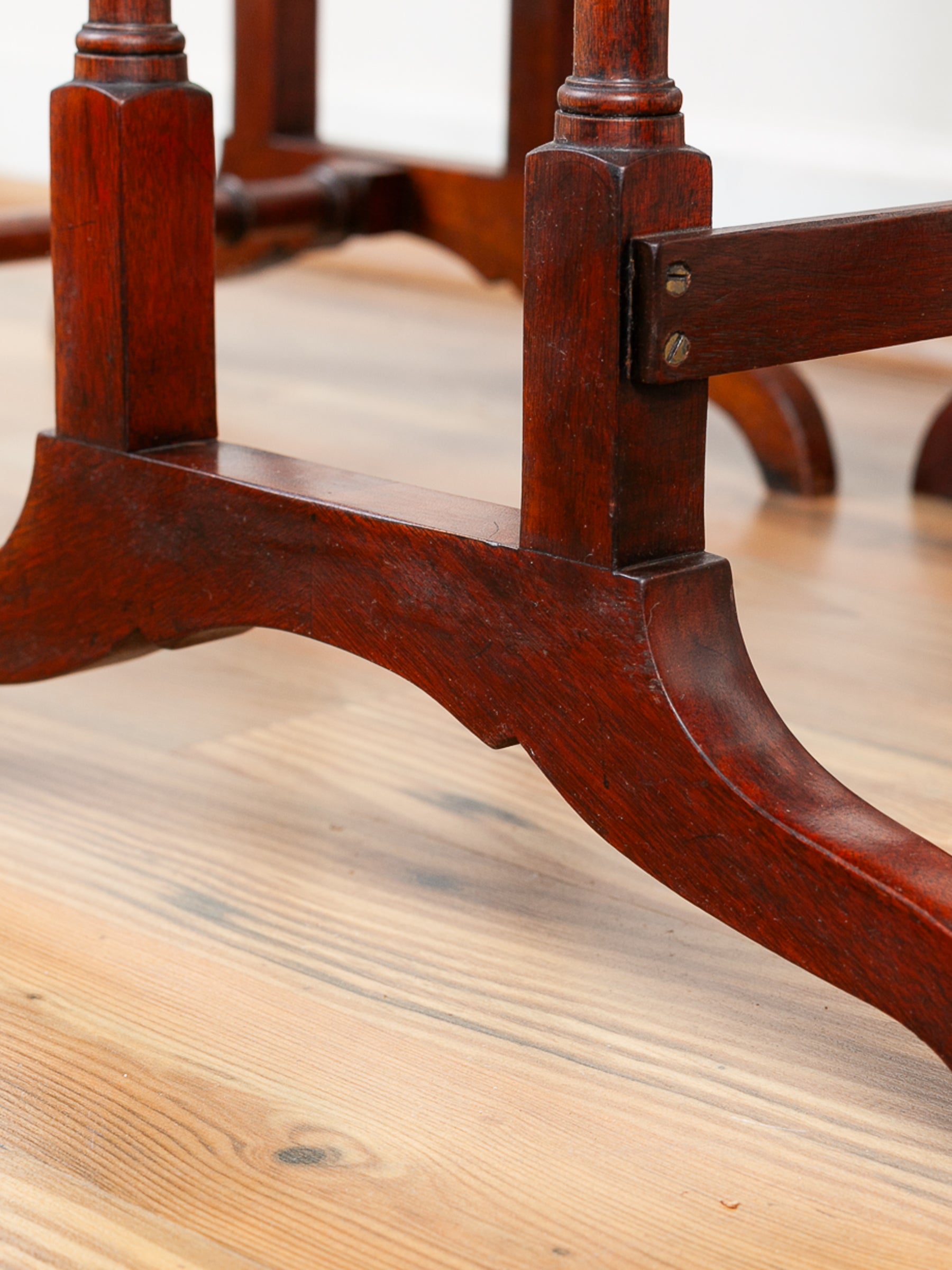 Close-up of a dark reddish-brown wooden table base with turned legs and metal brackets, resting on a light wood floor.