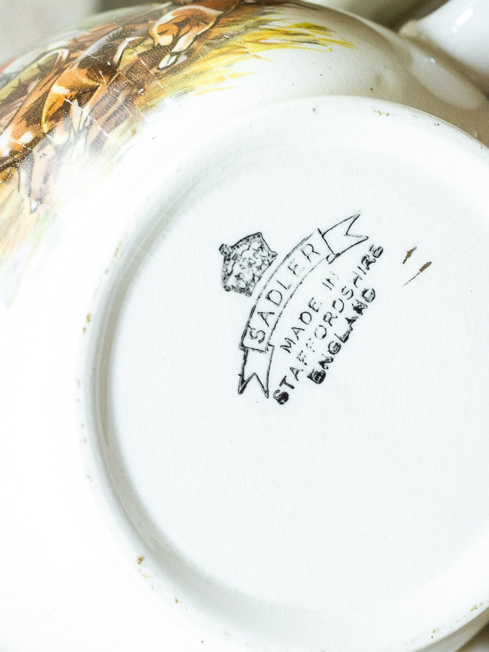Close-up of the bottom of a white ceramic teacup or mug, showing a printed maker's mark reading Sadler Made in Staffordshire England