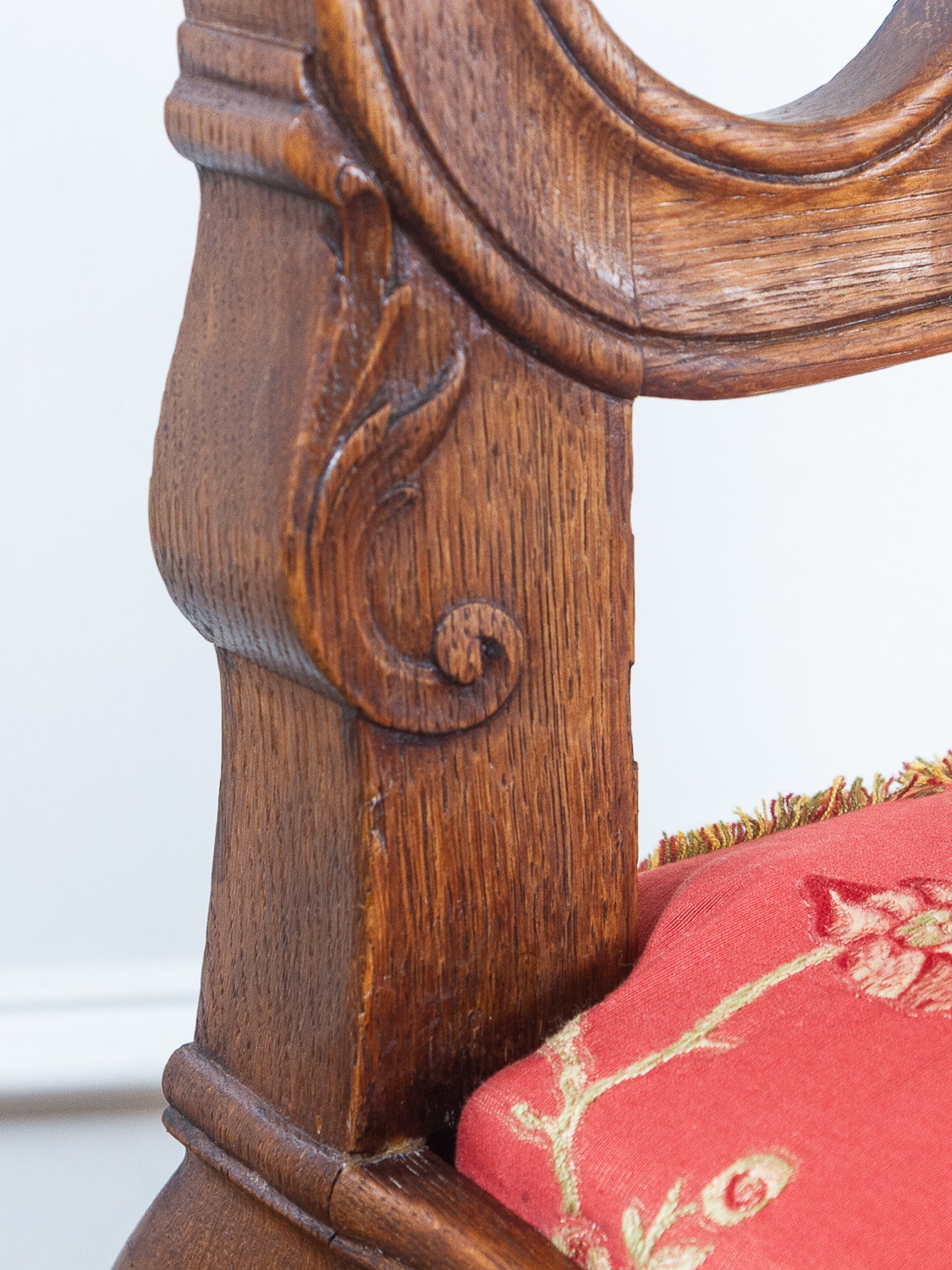 Close-up of an antique wooden chair's carved backrest post and red floral upholstered seat cushion.