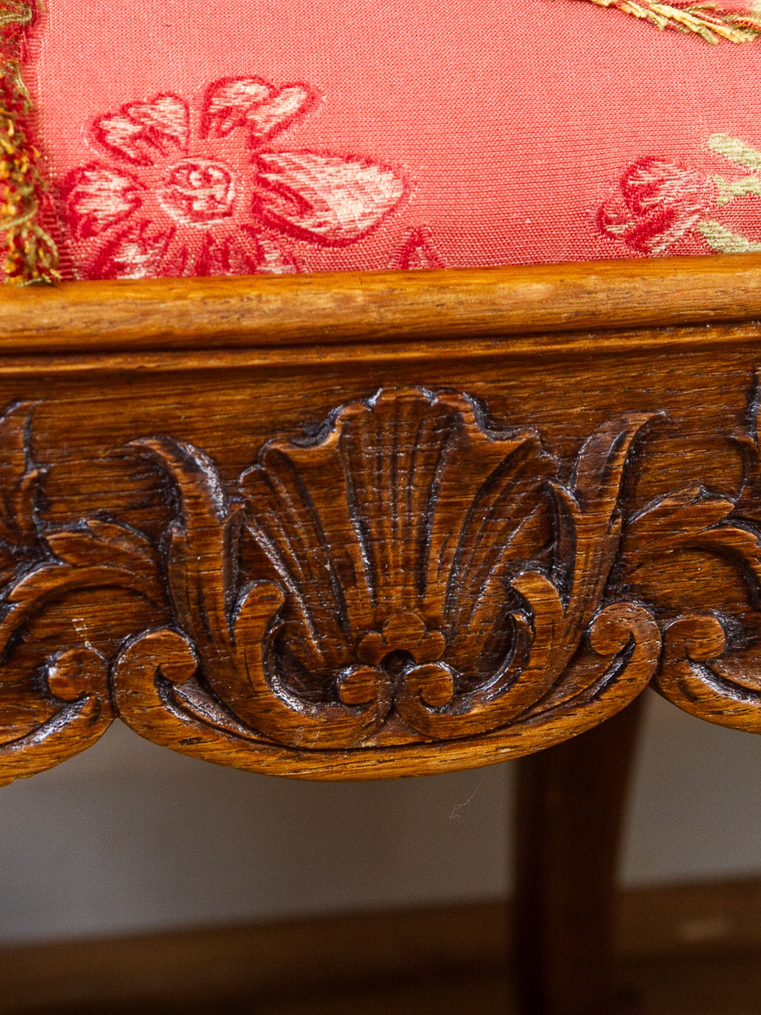 Close-up of an ornate carved wooden furniture leg with a red floral embroidered fabric cushion above it.