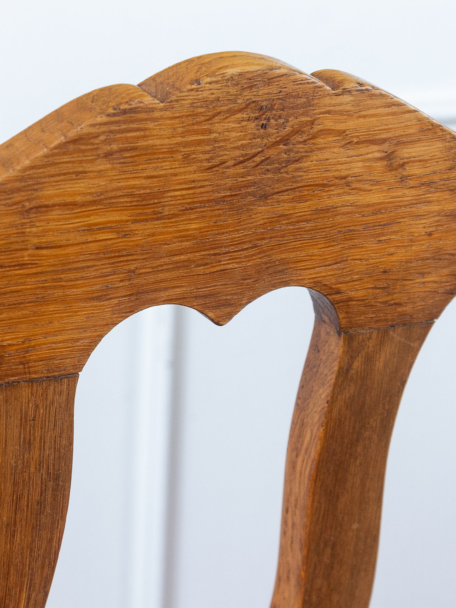 Close-up of back a wooden chair back showing the carved scalloped top rail and curved legs in a warm medium brown wood finish.