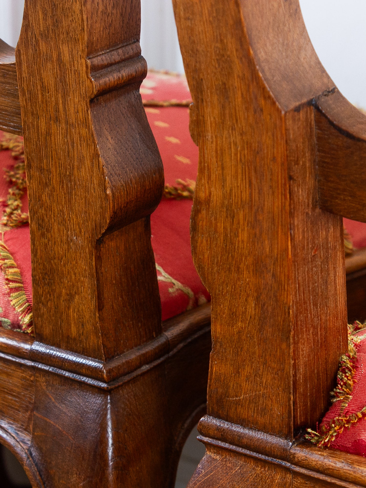 Close-up of ornate wooden chair legs with carved details and red upholstered seats trimmed with gold fringe.
