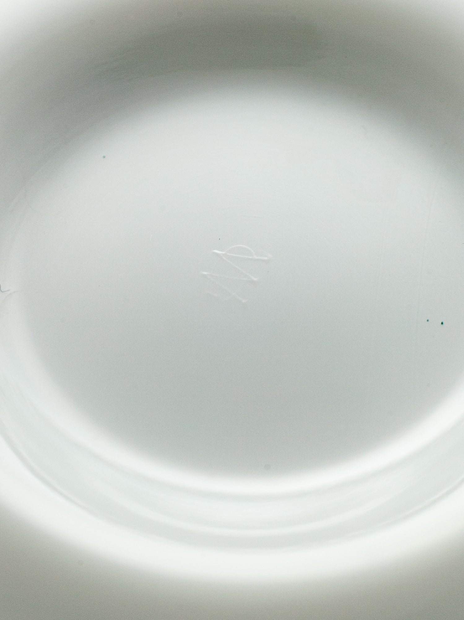 Close-up of the inside of a white milk glass plate or dish, showing a subtle embossed monogram for Westmorland Glass in the center.