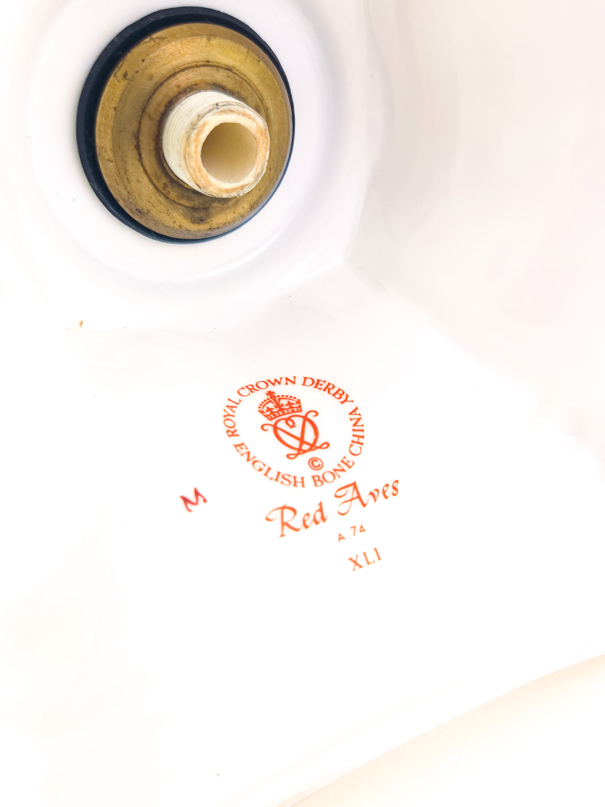 Close-up of a white ceramic candle stick holder showing the underside and red printed Royal Crown Derby 'Red Aves' mark on the bottom.