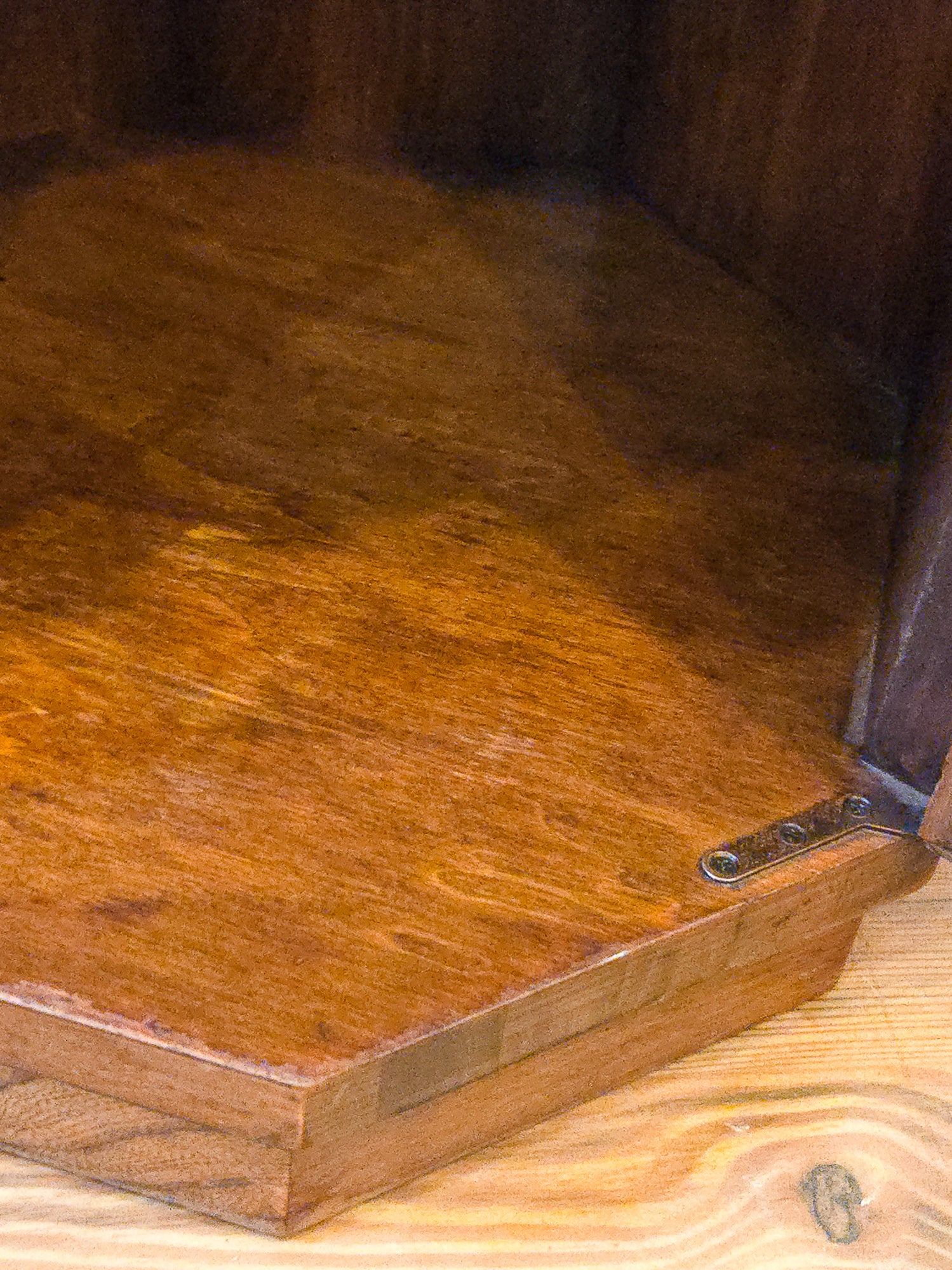 Close-up of inside the hexagonal cupboard a warm brown finish and a metal hinge, resting on a light wood surface.