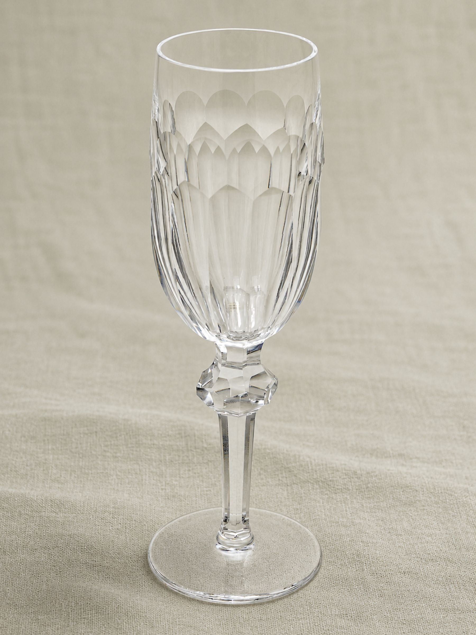 A clear Waterford Crystal Glass "Curraghmore" Design champagne flute with a textured, faceted pattern on the bowl and stem, set against a neutral beige fabric background.