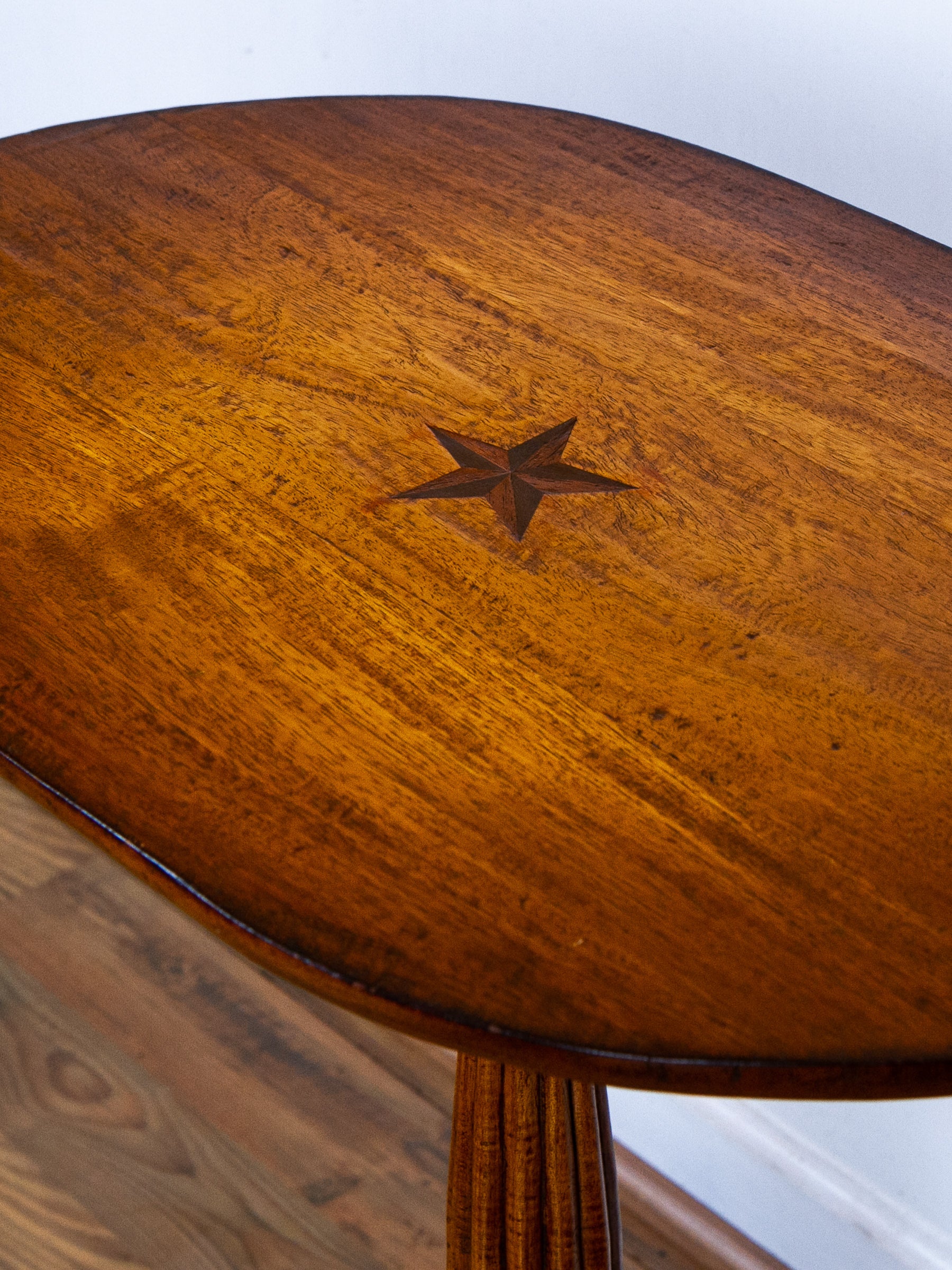 Close-up of a polished wooden table top with a star inlay at the center, showing rich warm brown wood grain and a matching wooden pedestal base.