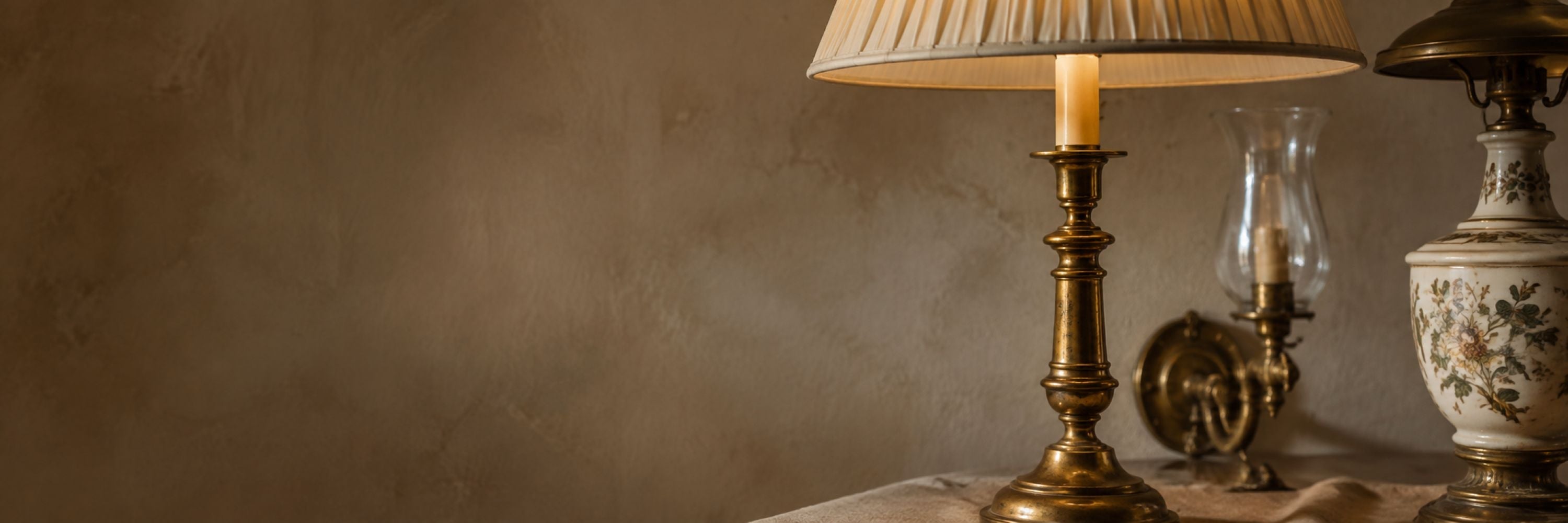 Antique brass table lamp, porcelain lamp and glass hurricane light arranged against a warm neutral backdrop.