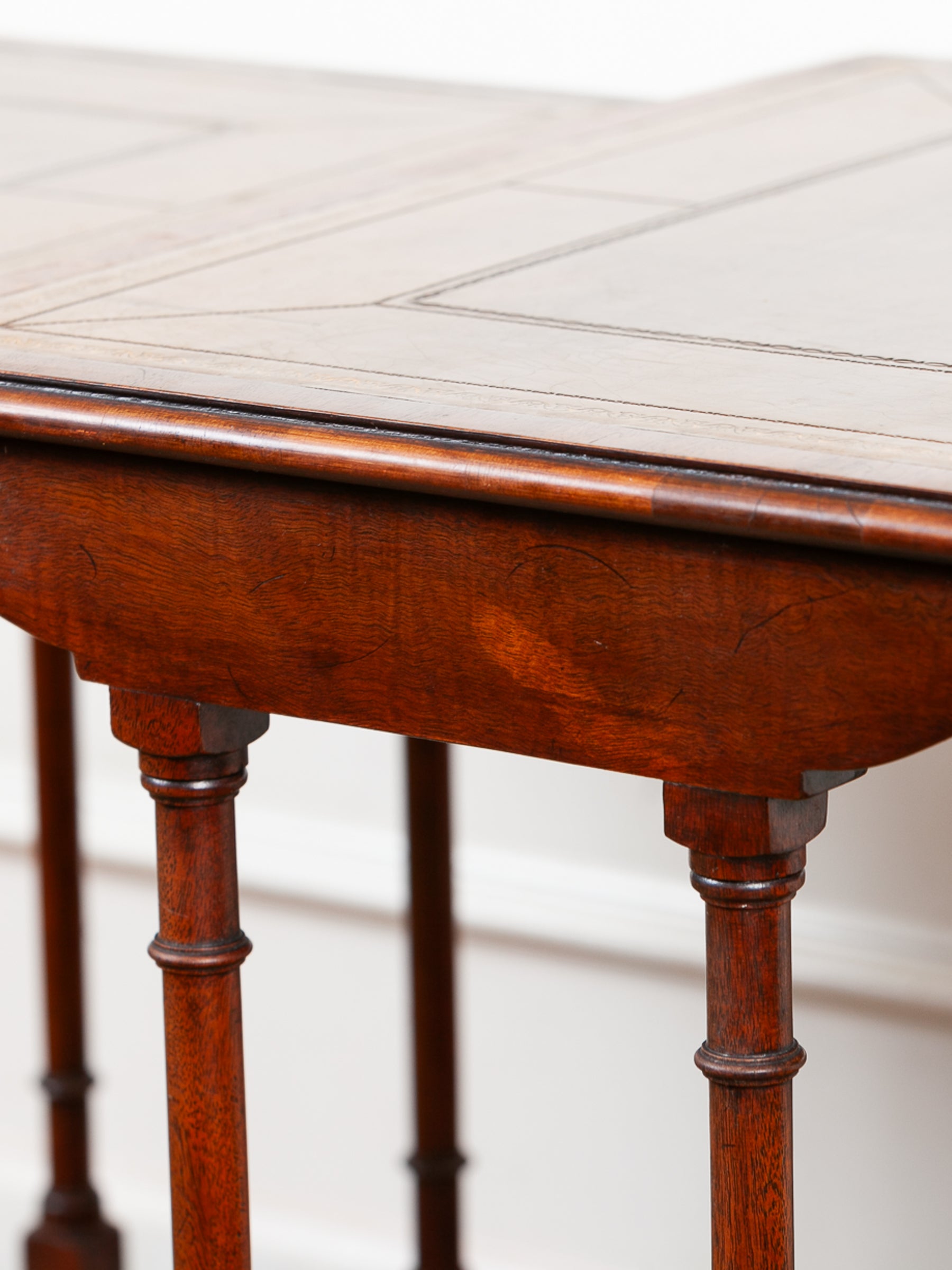 Close-up of a dark reddish-brown wooden table, showing the carved apron, turned legs, and part of the tabletop with inset panel lines.