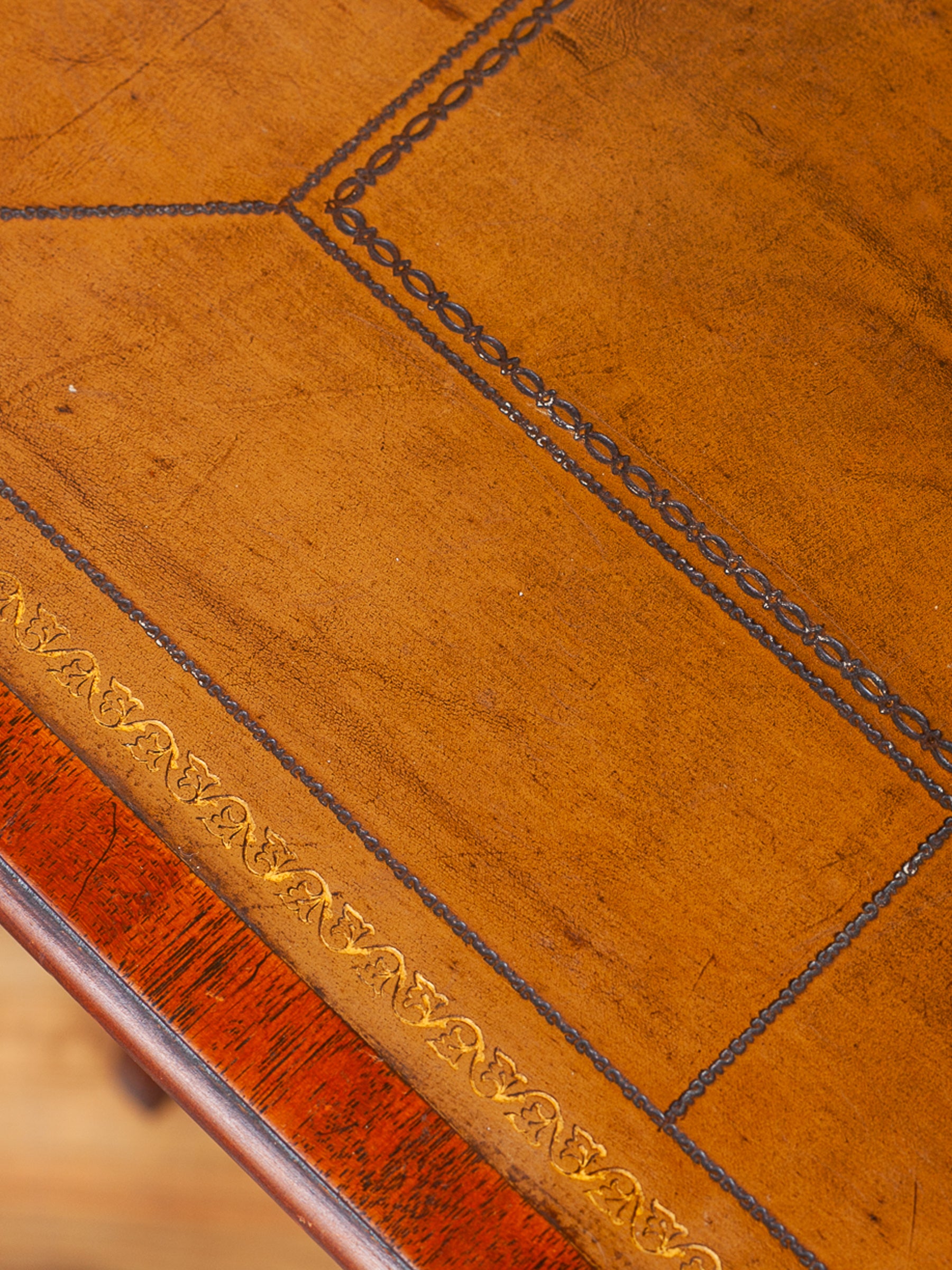 Close-up of a polished wooden leather table top with geometric inlay patterns and a reddish-brown wood edge.