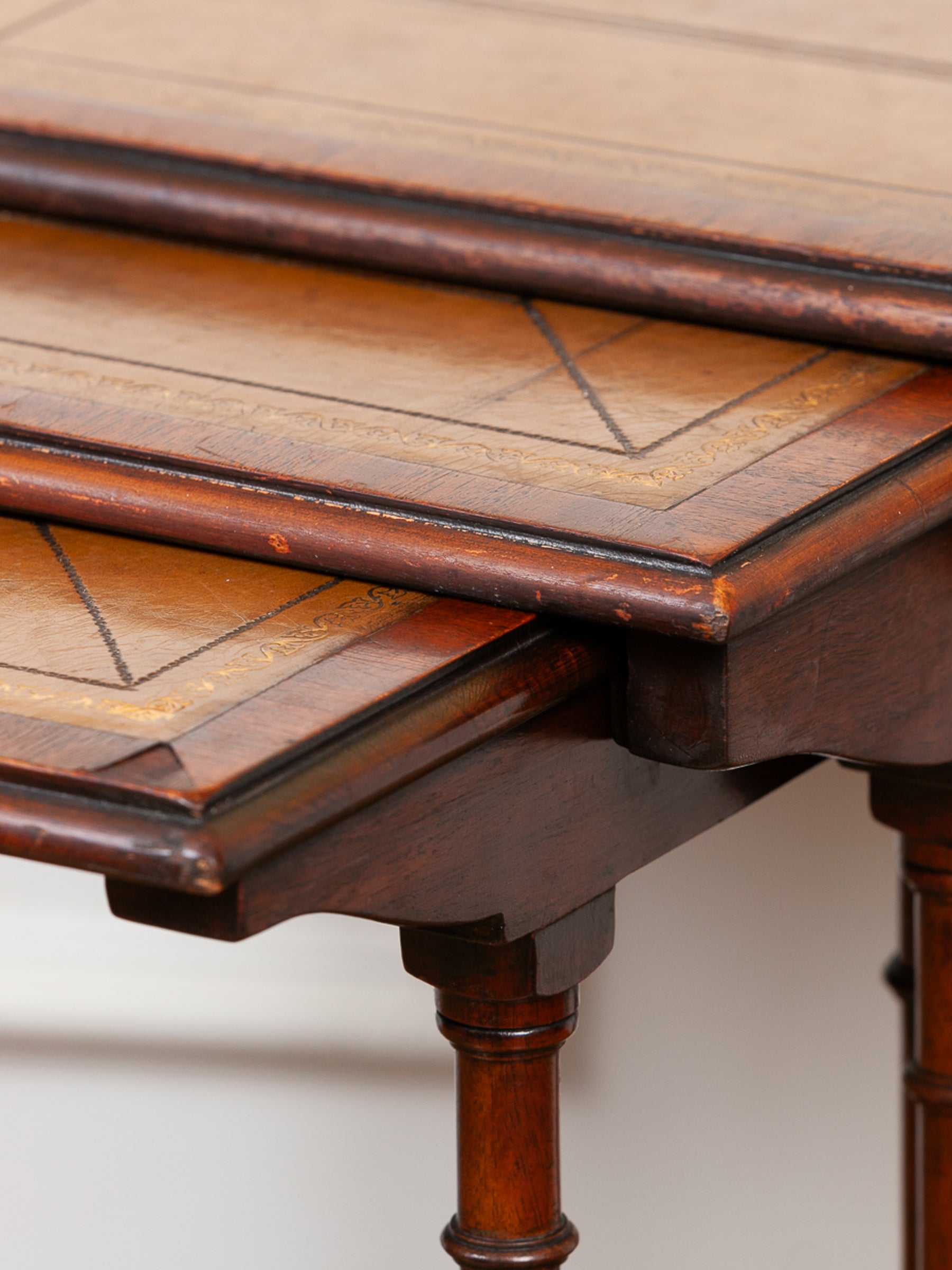 Close-up of a wooden nesting table with three tiers, featuring geometric tolled leather patterns and turned legs.