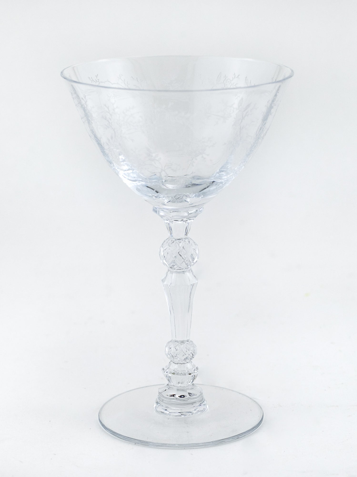 A clear glass coupe-style cocktail glass with an etched pattern on the bowl and a flared circular base, photographed against a plain white background.