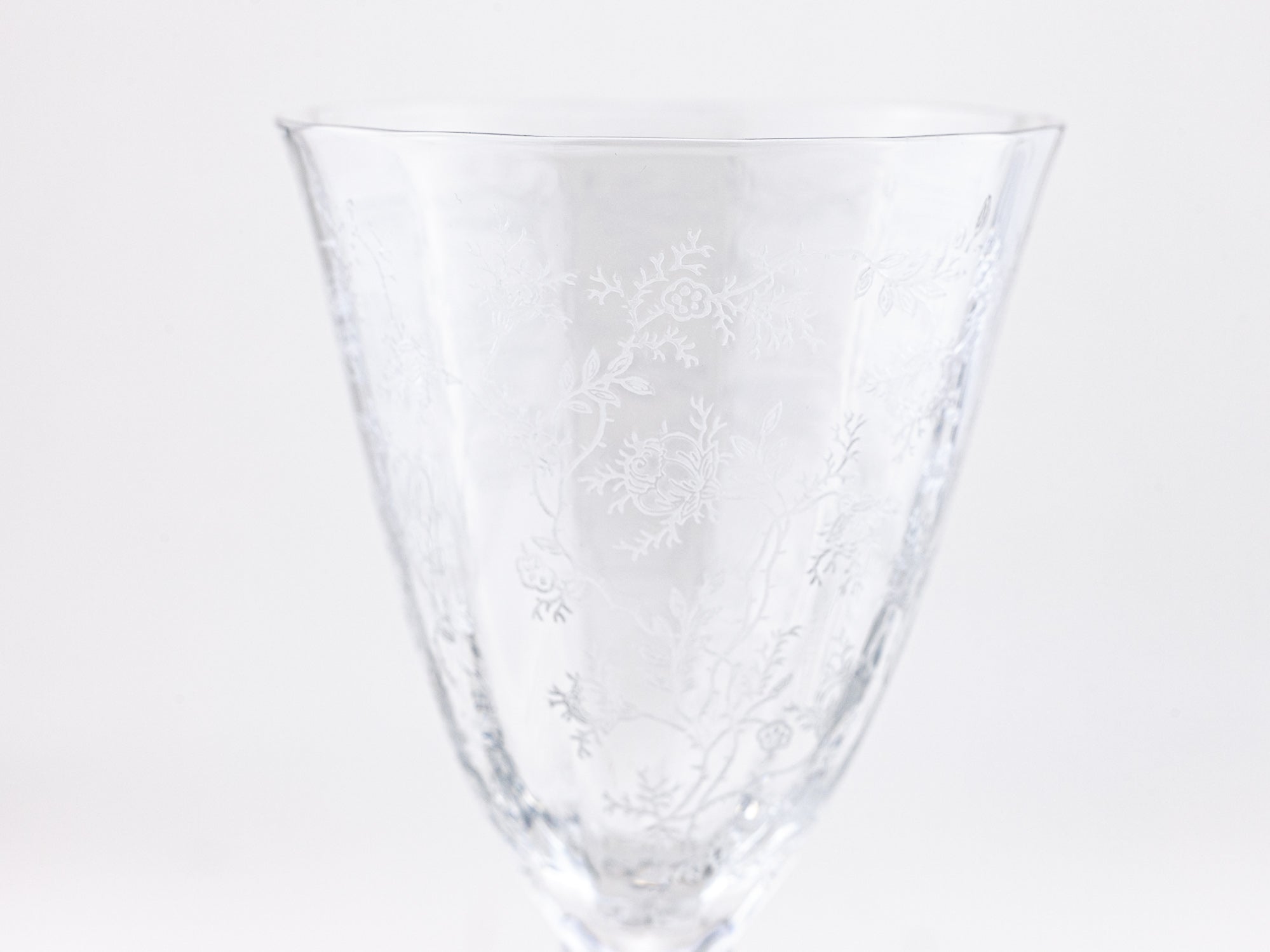A clear glass goblet with delicate white floral etched patterns, shown against a seamless white background.
