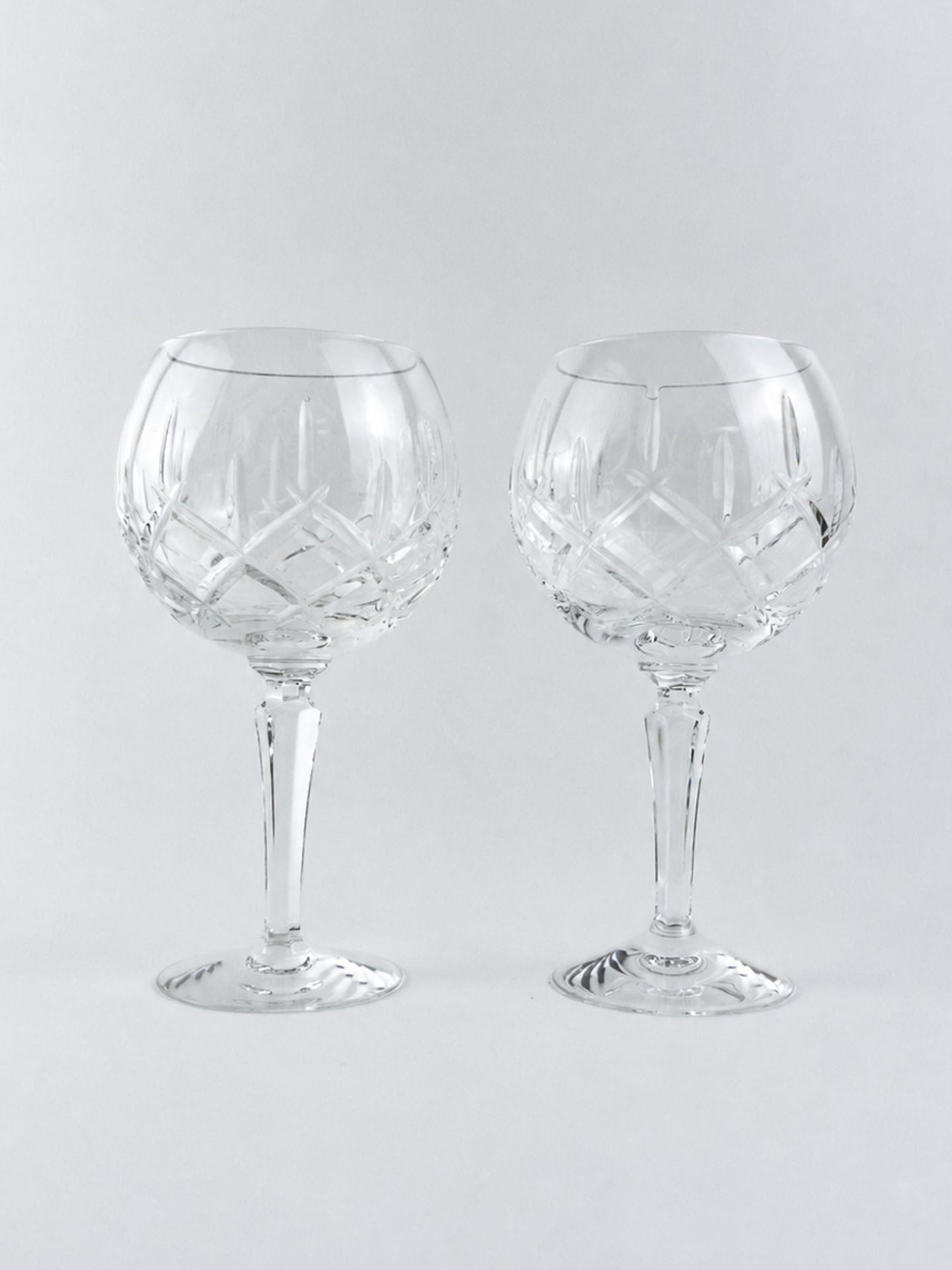 Two clear cut-crystal wine glasses with a diamond pattern, standing side-by-side on a light gray background.