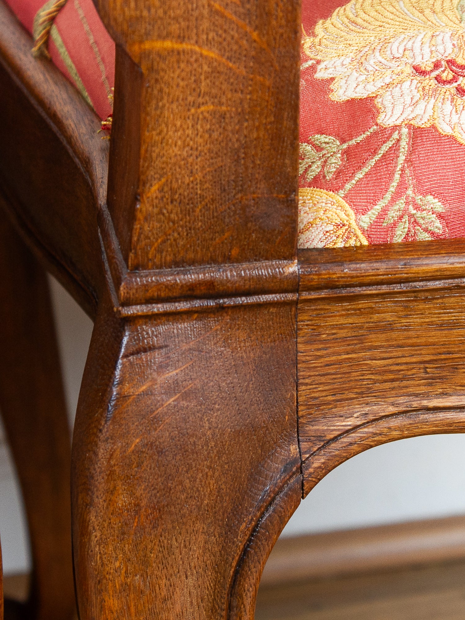 Close-up detail of an antique wooden chair showing the carved oak frame and red floral patterned fabric upholstery.