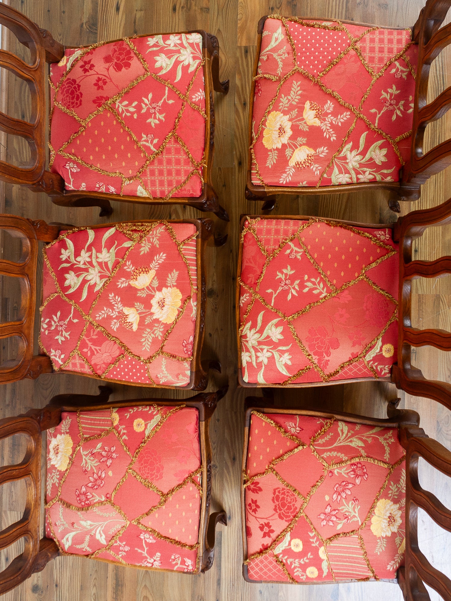 Six matching wooden dining chairs arranged in two columns on a wooden floor, featuring vibrant coral-red and pink floral upholstered seats with gold patterned trim.
