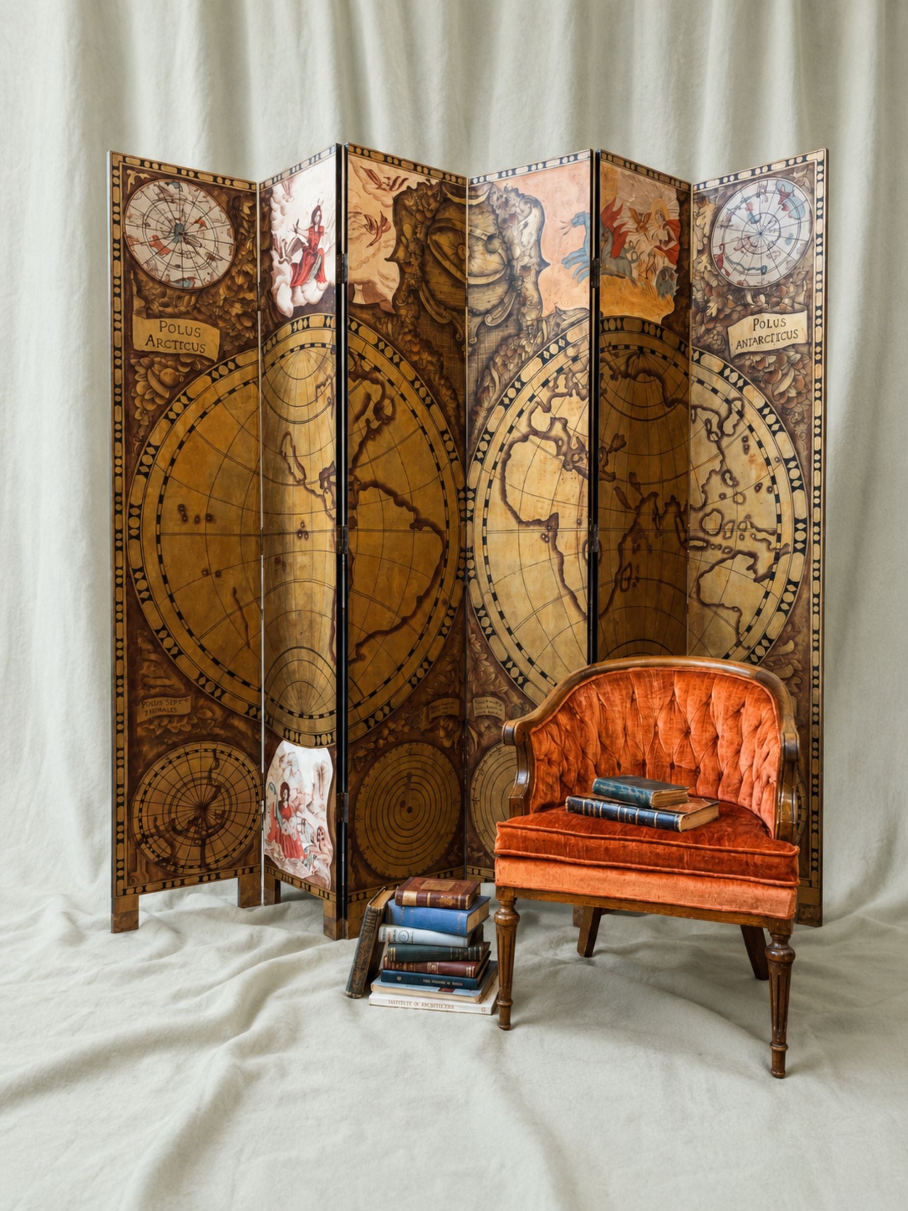 A vintage-style folding screen with an antique world map print stands next to an orange velvet armchair on a draped cream fabric backdrop.