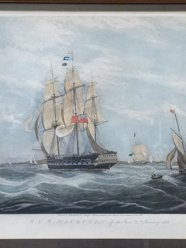 A framed historical nautical print depicting sailing ships on the sea under a cloudy sky, mounted on a textured yellow wall.