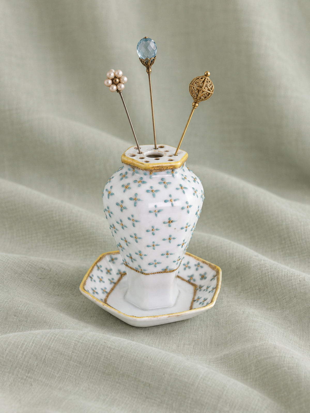 Antique Nippon porcelain hat pin holder with pale blue floral decoration, gilt accents and three decorative period-style hat pins.