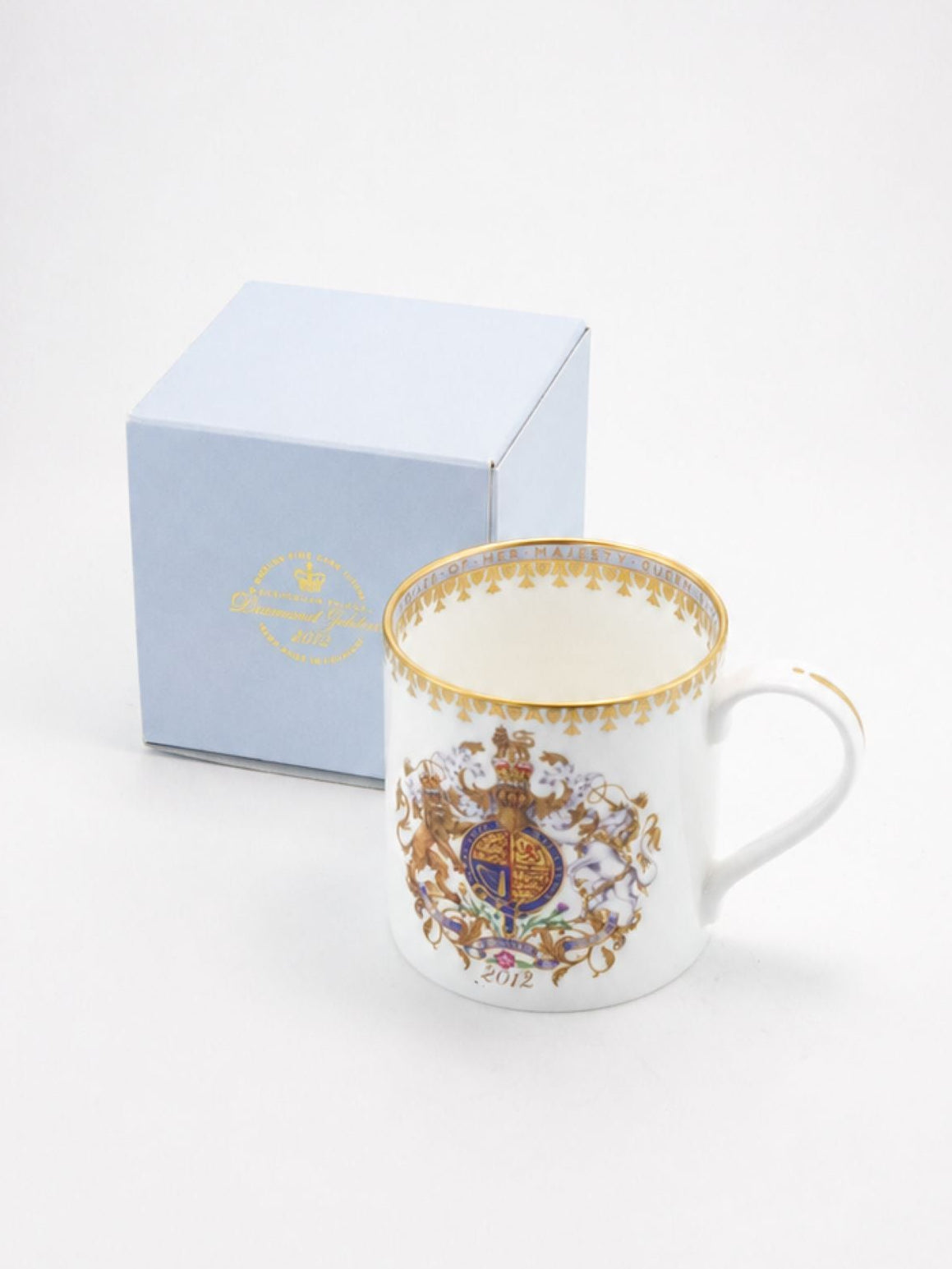 A white porcelain coffee mug with a gold-trimmed rim and a detailed multicolor crest on the side, shown next to its light blue presentation box on a white background.