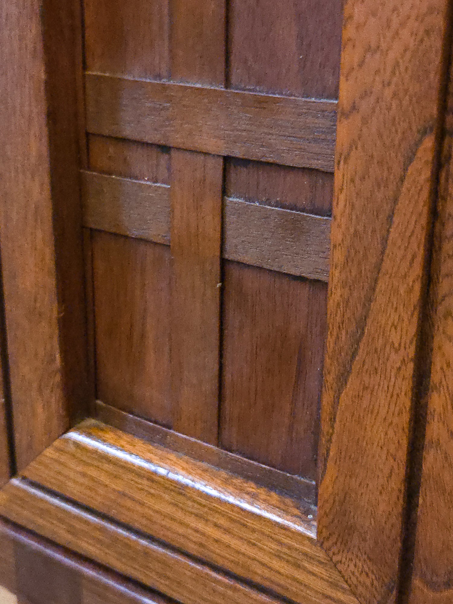 Close-up of a medium brown wooden cabinet door featuring a decorative geometric lattice pattern with raised paneling and a glossy finish.