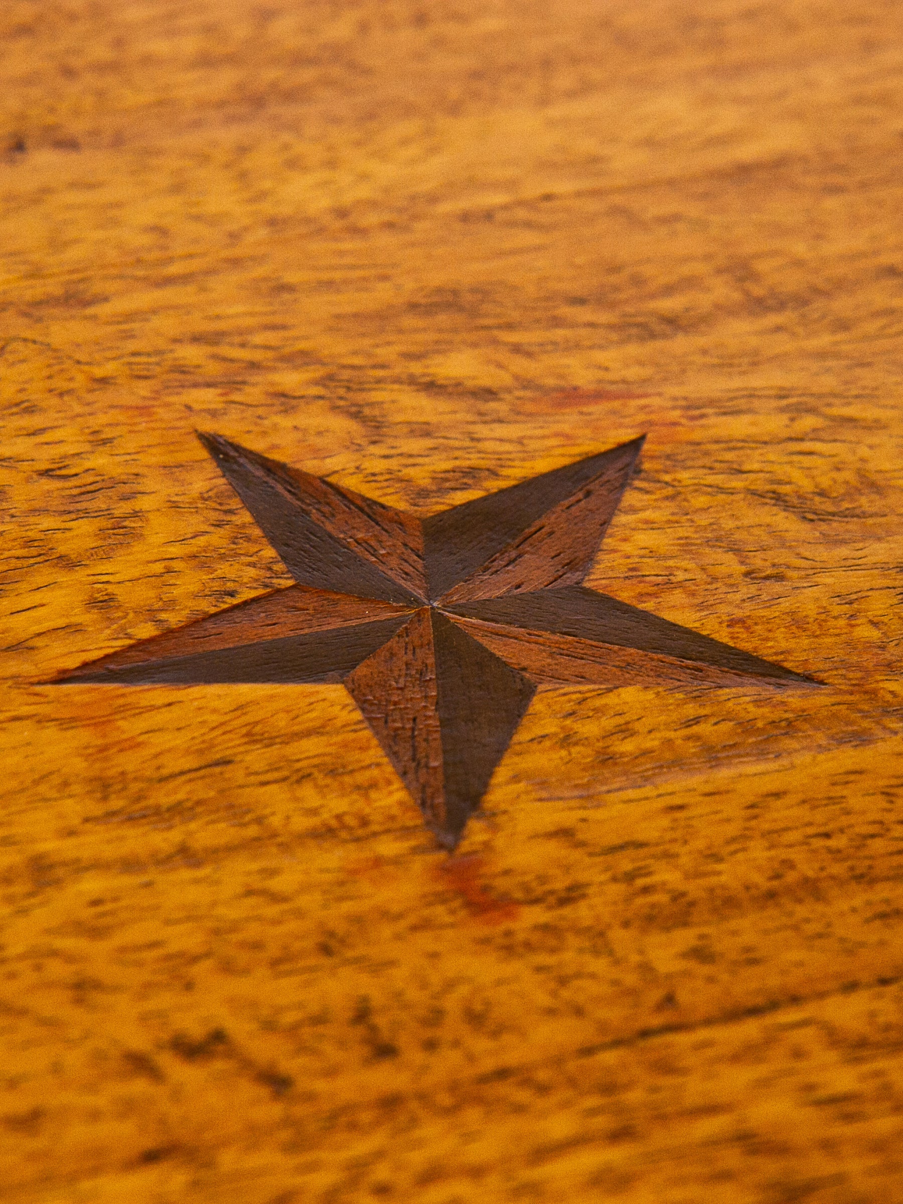 A close-up of a dark brown five-pointed star inlaid into a warm golden-brown wooden surface.